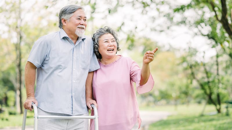 Happy Couple Man With Walker In Park Photo By Nontapan Nuntasiri Dreamstime. For article, At-home modifications for Parkinson’s help PD patients maintain safety and independence, through household, clothing, and dining adaptations.