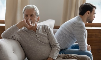 A mature man and his adult son have had a disagreement and are facing away from each other on a sofa. Image by Fizkes. Article offering tips on how to tell your adult children of a new relationship
