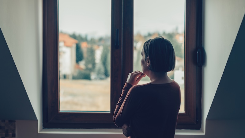 Mother staring out of a window wondering about her estranged son's choice