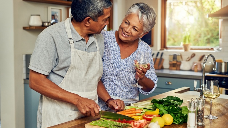 A couple cutting vegetables as a part of healthy eating. they're feigning happiness but you know they just want a burger.