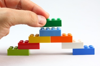 An adult hand stacking a Lego brick atop others, for an article on using Lego bricks to benefit people with dementia, Alzheimer’s, and other cognitive issues – as well as those in the general population