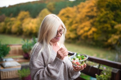 A senior woman outside eating a salad. Eating healthy is a way of protecting brain health. Image by Pojoslaw