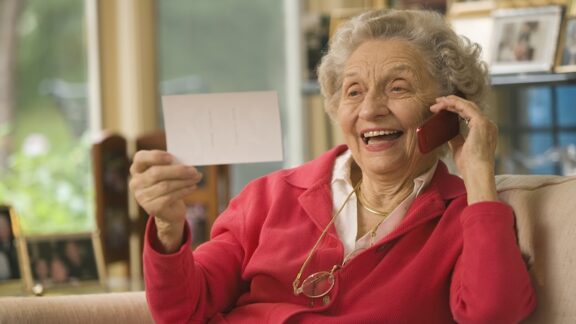 Woman talking on a cell phone, smiling, and looking at a picture. By Edward J. Bock 111. For article on best cell phones for seniors