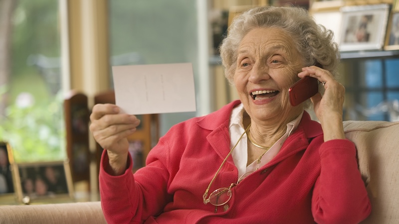 Woman talking on a cell phone, smiling, and looking at a picture. By Edward J. Bock 111. For article on best cell phones for seniors