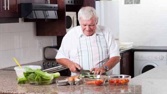 A man slicing vegetables in his kitchen. Image by Hongqi Zhang. Article on healthy meals for seniors who live alone