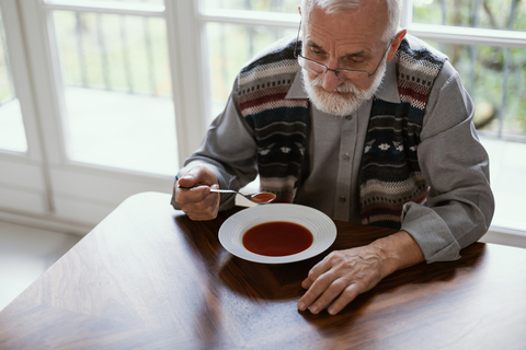 A man seems to have no appetite as he hesitates to eat his soup. Image by Katarzyna Bialasiewicz. Article on eating disorders among seniors 