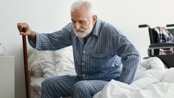 A weak senior man struggling to stand up from his bed. Is he ready for a disaster or does he need emergency preparedness planning for seniors? Image by Katarzyna Bialasiewicz