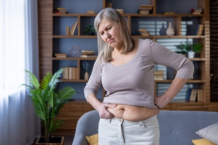 Belly fat is a nearly inevitable sign among changes of aging, as this woman expresses her frustration with her belly, squeezing the fat. Image by Liubomyr Vorona 