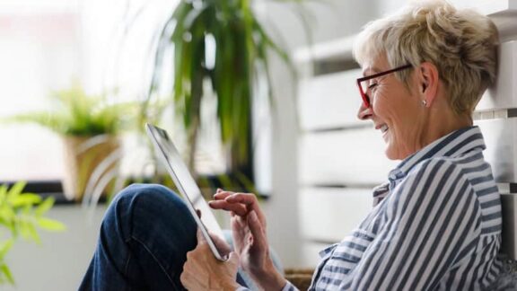 Woman sitting on her porch playing crossword puzzles for seniors on her tablet