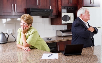 A couple looking away in a kitchen because they're fighting. This old friend's new husband is attempting to control her.