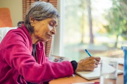 Woman writing a list, as of ways that her husband and friends can help her with her isolation as a result of her Alzheimer's disease diagnosis. Image by Paul Maguire.