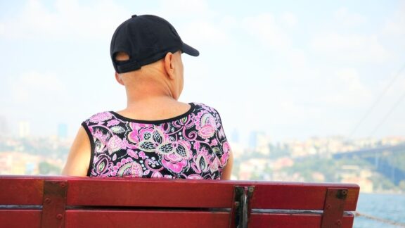 A woman with cancer sits alone on a park bench, contemplating that some friends withdraw after a terminal diagnosis