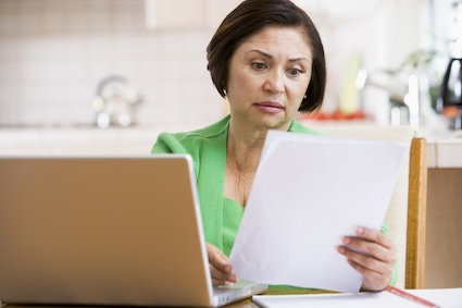 Woman using computer and looking at a piece of paper with concern, trying to choose the best Medicare plan. Monkey Business Images