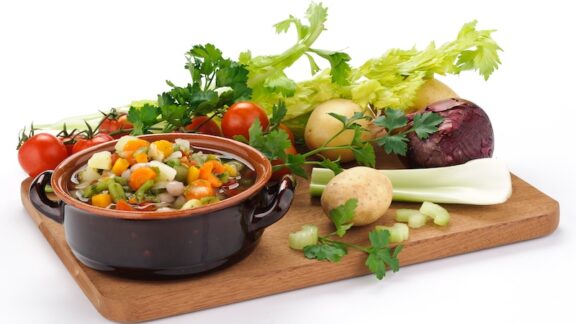 A cutting board with both cooked vegetables and raw vegetables.