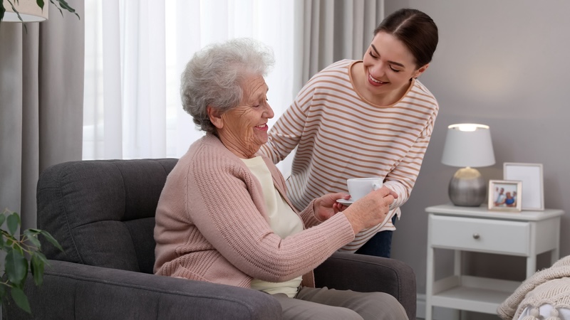 Young woman giving coffee to her seated grandmother. For article, is memory care tax deductible? Image by Chernetskaya