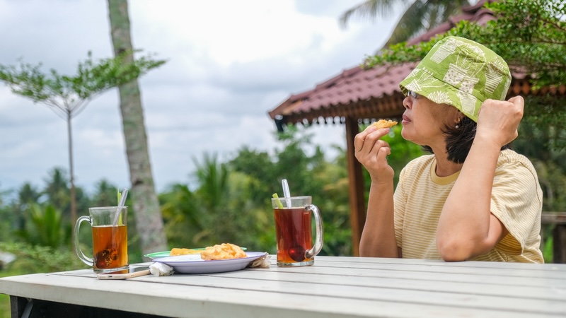 Woman eating a snack at a table outside in the village of Yogyakarta, Indonesia. The villages make it possible to have international retirement on a budget