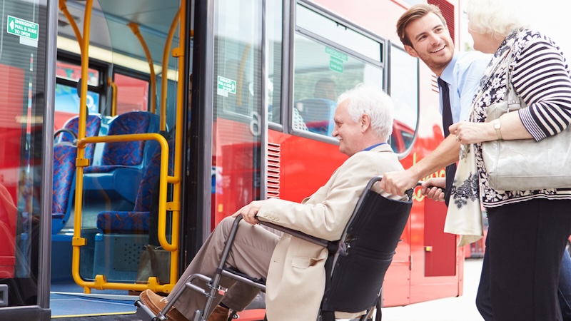 A man helps a senior couple, with the man in a wheelchair, onto public transportation. For From Rideshares to Shuttles: Navigating Transportation Services for Seniors. Image by Monkey Business Images