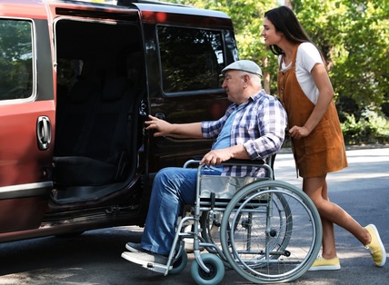 A young woman working for paratransit helps a man in his wheelchair to the van. Image by Chernetskaya. From Rideshares to Shuttles: Navigating Transportation Services for Seniors