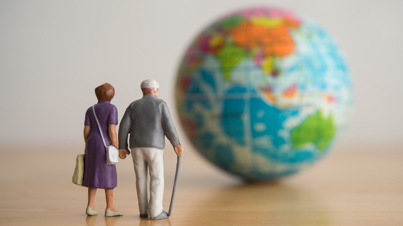 Plastic people - a senior couple - walking toward a small globe, for article on moving abroad in retirement. Image by Pla2na
