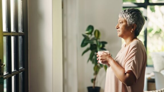 A woman with her coffee looks out of her window. Peaceful morning habits for seniors can set a positive tone for the rest of the day. Image by Yuri Arcurs