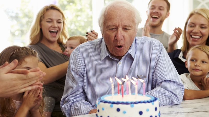 Man blowing out his birthday candles, surrounded by families, making dreams come true.