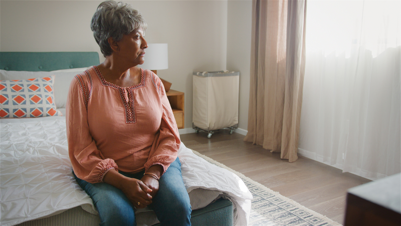 After losing a life partner, this senior woman grapples with sadness, sitting alone on her bed.