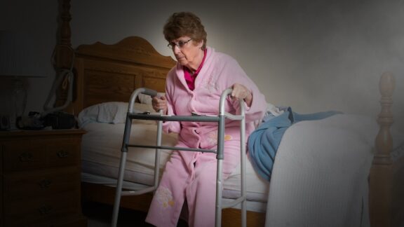 A woman having difficulty getting out of bed and using her walker, wondering if it is time for assisted living. Image by Wisconsinart