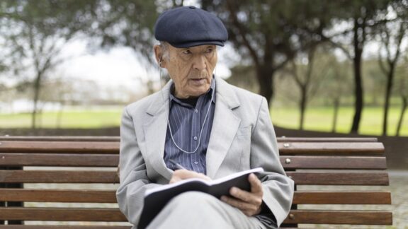 A man sitting on a park bench tracking life in his journal. Image by Konstantin Shishkin
