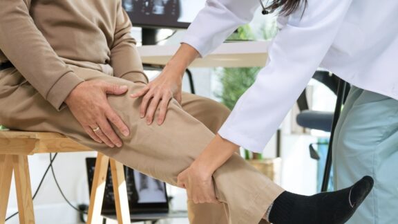 Man with doctor holding his knee because of osteoarthritis