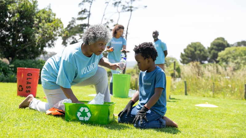 Senior woman and young boy working together outside, picking up litter for recycling, demonstrating the benefits of intergenerational programs.