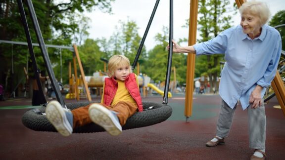 Senior woman swinging a child at a playground, demonstrating the benefits of intergenerational programs. Image by Marysmn