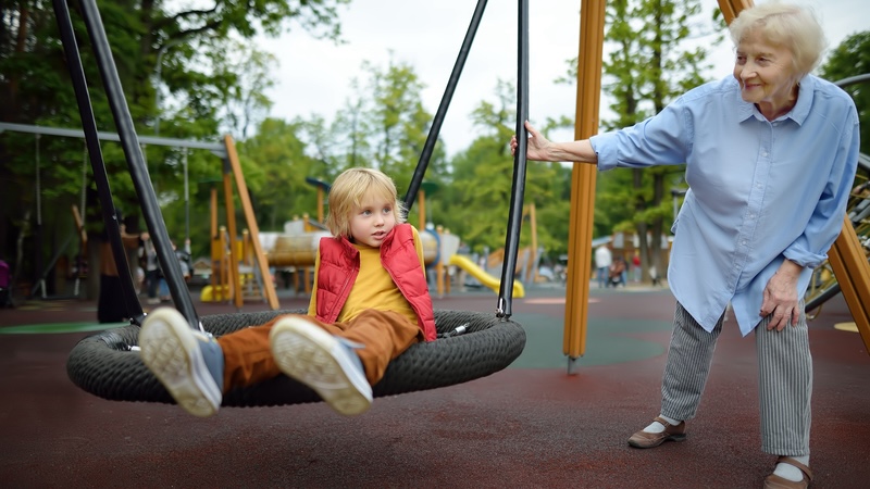 Senior woman swinging a child at a playground, demonstrating the benefits of intergenerational programs. Image by Marysmn