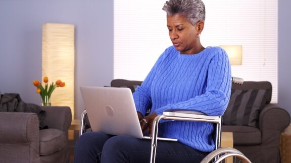 Woman in wheelchair on computer learning about how insurers are scaling back on Medicare Advantage.