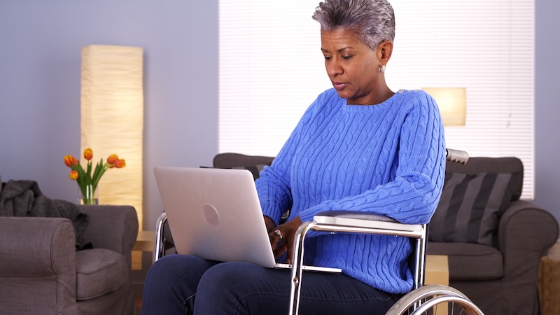 Woman in wheelchair on computer learning about how insurers are scaling back on Medicare Advantage.