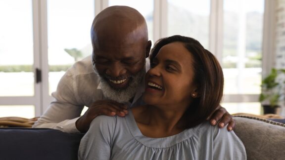 Older couple gently touching and smiling. Renouncing traditional expectations, many seniors are redefining love relationships, whether they’re aging in place or in a senior community. Image by Wave Break Media Ltd