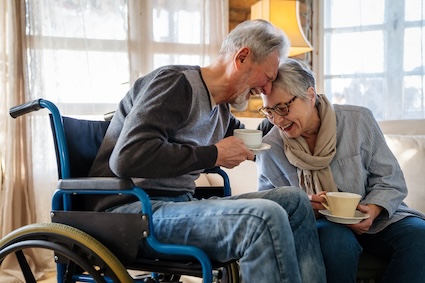 A man in a wheelchair and his partner sip coffee and laugh together. Renouncing traditional expectations, many seniors are redefining love relationships, whether they’re aging in place or in a senior community. 