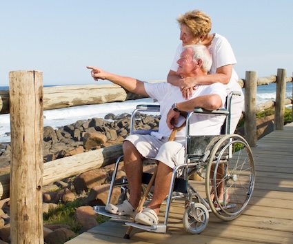 A happy retired couple, man in a wheelchair and woman behind him, have overcome the the emotional challenges of a staggered retirement. Image by Hongqi Zhang