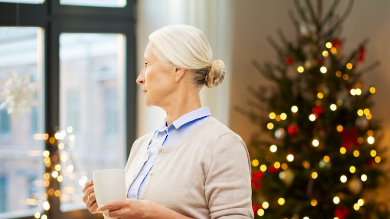A woman looking sad by a Christmas tree experiencing Christmas disappointment.
