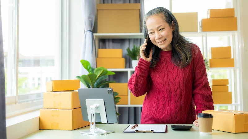 A senior woman on the phone, and a lot of boxes, starting a successful business