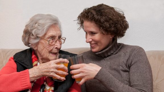 A young woman believes in checking in on seniors, and is visiting with an elderly neighbor. Image by Peter Maszlen.