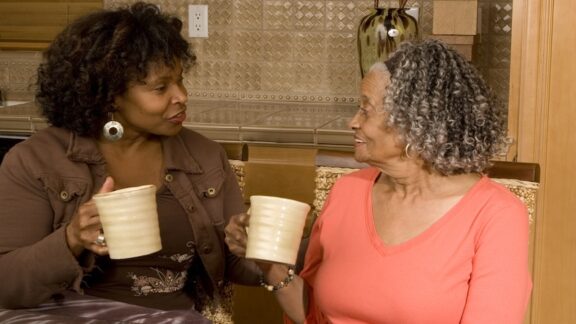 African American woman drinking coffee with her elderly mom even though it hurts your wallet.