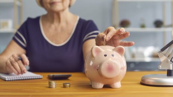 A woman putting coins in a piggy bank wanting to trim her monthly budget.