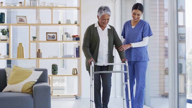 In-home caregiver helps a woman using a walker, by Yuri Arcurs. Article on the growing caregiver shortage