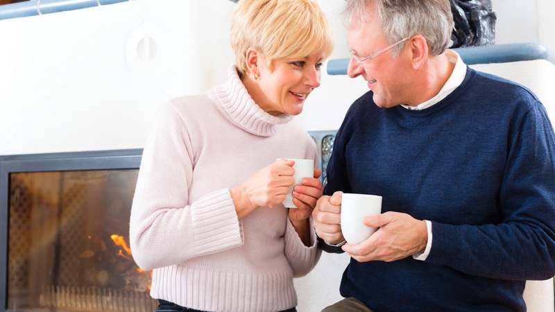 Senior couple enjoying the health benefits of coffee and tea by drinking some next to a fireplace.