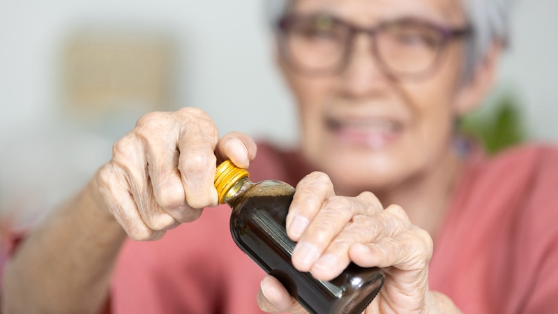 A senior woman is having a hard time opening a small bottle. Age and infirmities can make bottles, jars, and clamshell wraps challenging to get into. Gardgets and tips for tackling hard-to-open packaging can help. Image by Satjawat Boontanataweepol