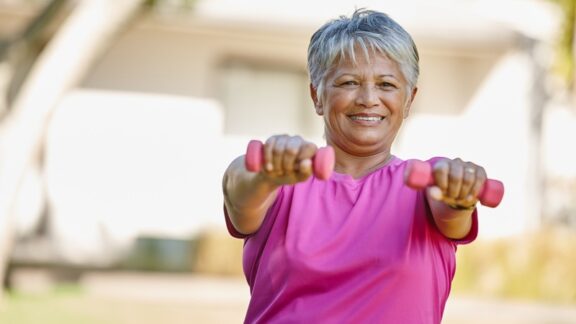 A senior woman outside holding light weights in front of her, knowing that isometric exercises can lower blood pressure. Image by Yuri Arcurs