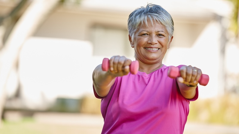 A senior woman outside holding light weights in front of her, knowing that isometric exercises can lower blood pressure. Image by Yuri Arcurs