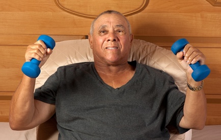 Man resting in bed but using weights, since isometric exercises can lower blood pressure. Image by Zafi123