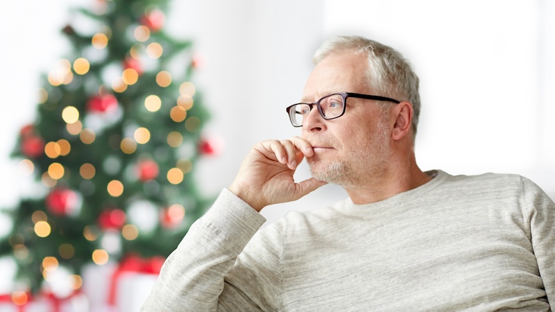 Sad man in front of a Christmas tree, needs help navigating grief during the holidays. Image by Syda Productions