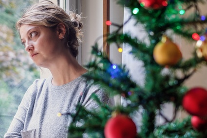 A sad woman by a Christmas tree, needing help managing grief during the holidays. F01photo